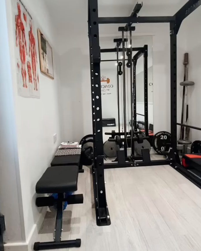The squat rack with its cable pulley, weight plates and a bench in Carly's studio.